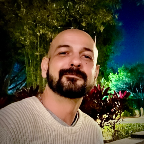 Professional headshot of a systems administrator with 20 years of IT experience, smiling warmly at the camera in a neutral office setting, conveying approachability and technical expertise